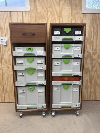 Two shop-made hardwood cabinets on locking castors, each holding a column of Festool Systainers on SYS-AZ pull-out drawers, with one orange Fein case in the right-hand cabinet