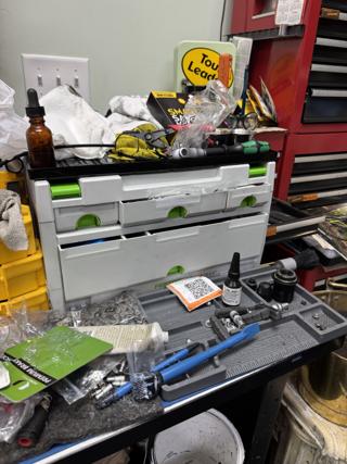 Light grey Festool-liveried Drawer-systainer III with green latches at the back of a bike shop workbench, small drawers above and a deep drawer below, surrounded by headset bearings, a rivet tool, brushes and a bench mat