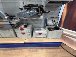 Close view of light grey Mafell cases of different heights with red catches and the mafell logo stamped on their lids — stacked systainer T-Locs on the left, a MAX3 with the rounded Systainer³ catch in the middle, and one open on the right showing black foam cut for a saw