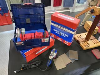 Blue systainer open on a table showing red foam sanding pads and film sheets standing on edge in blue foam, labelled 3x4, with a SurfPrep Surflex Foam Roll carton and a blue 3x4 electric sander beside it