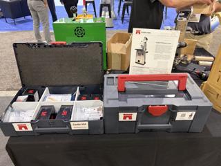 Two anthracite systainers with carmine red catches side by side on a black table, the left one open with white divider trays holding Castle USA wood plug sample cards and black screw boxes, the right one closed with a red lid handle and a Castle 110 Pocket Cutter label