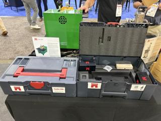 The two anthracite Castle USA systainers on the table with the right one now open, showing dark foam in the lid and a moulded tray in the base holding a small Castle-branded box and a sample block, with a TSM-12 spec sheet and the green machine behind