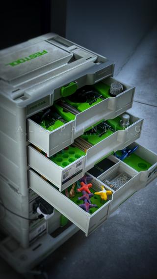 A three-drawer Festool Sortainer, open, showing green 3D-printed inserts holding airless spray guns and accessories