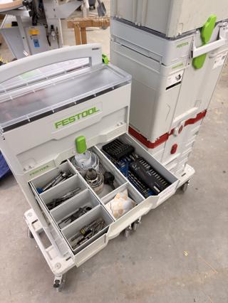An open Festool Sortainer drawer holding hole saws, drill bits, driver bit sets and felt pads, with a red-banded Lamello systainer stacked alongside