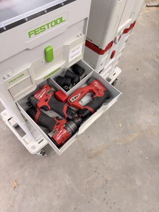 A Sortainer drawer holding three Milwaukee M12 tools — a drill, an installation driver and a hydraulic driver — with the installation driver's spare chuck heads in the compartment behind them