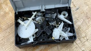 An open light grey Systainer³ XXS filled with assorted radio control parts — white and black servo arms, gears, shock mounts and small screws