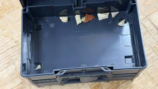 Small slivers of wood broken out of hand-cut dovetails, resting inside an open anthracite Systainer³ XXS